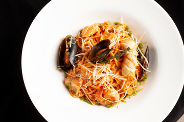 Pasta with seafood and cheese in a plate. On a dark background.