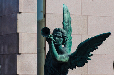La statua bronzea di un angelo che suona la tromba su una tomba dell cimitero maggiore di Milano - obrazy, fototapety, plakaty