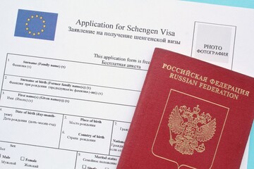 Schengen visa application form in English and Russian language and passport on blue background....