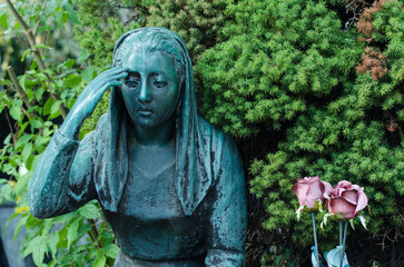 Primo piano di una statua bronzea di una donna dolente su una tomba del cimitero maggiore di Milano