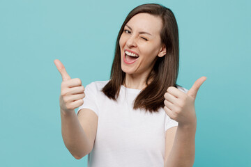 Young satisfied smiling cheerful caucasian woman 20s wear white t-shirt show thumb up like gesture wink isolated on plain pastel light blue cyan background studio portrait People lifestyle concept.