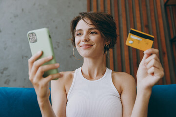 Young woman wear white tank shirt using mobile cell phone hold credit bank card shopping online...