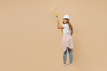 Back view full size young employee laborer handyman woman in white t-shirt helmet use roller paint walls isolated on plain beige background Instruments accessories for renovation room Repair concept.