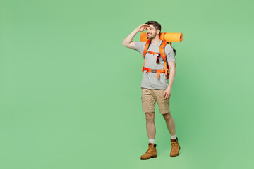 Full body young traveler white man carry backpack stuff mat walk look far away distance isolated on plain green background Tourist leads active healthy lifestyle. Hiking trek rest travel trip concept