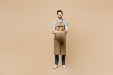 Full size fun young man barista barman employee wear brown apron work in coffee shop hold italian...