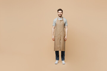 Full body smiling fun young man barista barman employee wear brown apron work in coffee shop look camera isolated on plain pastel light beige background studio portrait Small business startup concept.