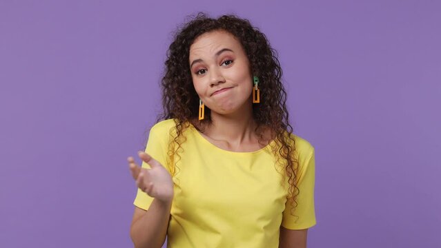 Young fun confused shy shamed woman of African American ethnicity 20s she wear yellow t-shirt look camera spreading hands say oops ouch oh omg i am so sorry isolated on plain pastel purple background