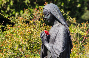 Primo piano di una statua bronzea di una donna dolente  con un fiore in mano su una tomba del...