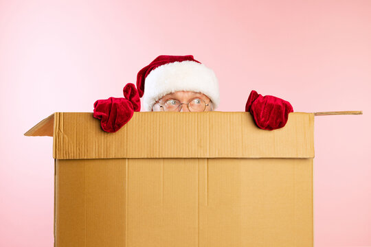 Portrait of senior man in image of Santa Claus hiding inside cardboard box. Presents, gifts for holidays