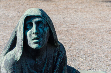 Fototapeta na wymiar Primo piano di una statua bronzea di una donna dolente con un fiore in mano su una tomba del cimitero maggiore di Milano