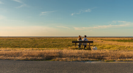 People (couple) sit on a bench in the middle of nowhere. Flat, remote, peaceful, meadow landscape.