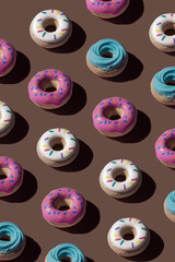 Trendy sunlight seamless pattern made of three colorful doughnut toys with sharp shadow on brown chocolate background. Minimal food summer concept with copy space.