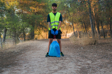 Man in a reflective vest and gloves with a plastic bottle and a trash bag in the forest