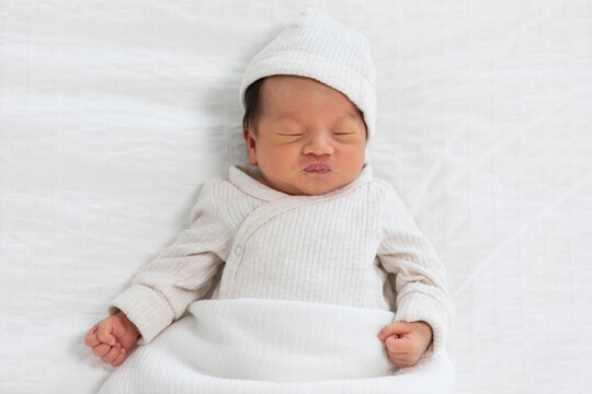 Top view happy newborn baby lying sleeps on a white blanket comfortable and safety at warmth place. Cute Asian newborn sleeping and napping on bed. Newborn Baby Care concept