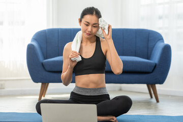 Fototapeta na wymiar Athlete Asian young woman take a break during exercise online class on exercise mat at home.Healthy female in sportswear relax after workout exercise finished.Cardio Exercise Concept