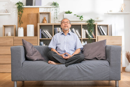 Mature Asian Man Doing Yoga For Meditation On Yoga Mat In Living Room At Home.Clam Of Senior Or Elderly Men Meditation Deep Breath And Relax At Cozy Home.Happy Retired Meditation At Home Concept