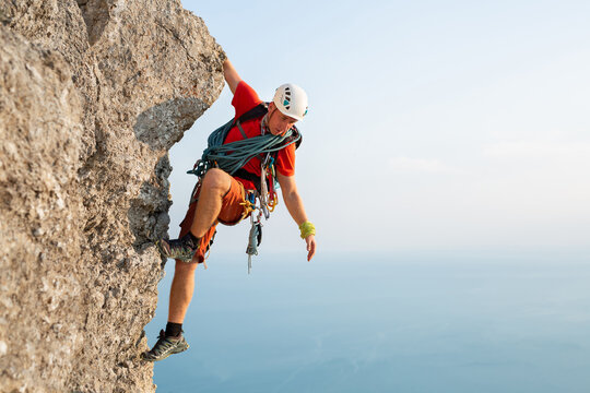 Young male climber climbs a difficult route with a view of the sea at sunset.