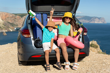 Children are sitting in the trunk of a car with suitcases, inflatable circles near the sea.