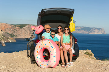 Happy family is sitting in the trunk of a car with a sea view.