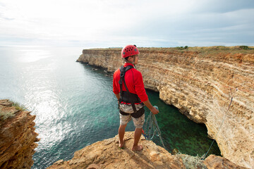 Portrait of a man in protective gear and helmet on the edge of a cliff. View from the back. Rope jumping.