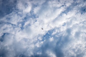 The plane on a background of the blue sky with clouds. Plane silhouette in the center of the photo frame
