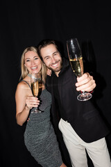 Positive couple looking at camera while holding glasses of champagne isolated on black.