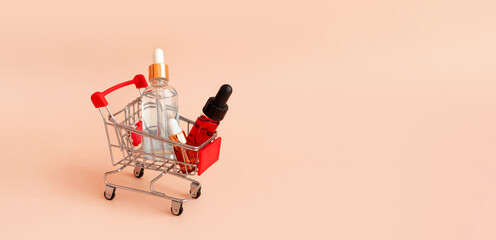 Online shopping minimalistic concept. Small cart with cosmetic bottles. Essential oil, serum and peeling gel in glass droppers. Mixture of beauty products.