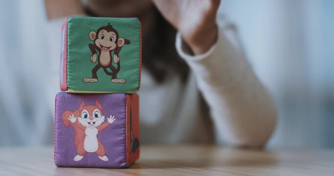 Two children's plush cubes with images of a squirrel, an elephant and a monkey. A girl puts one cube on another. Close-up. 