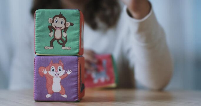 A girl speaks to someone and puts the children's plush cube with the image of a monkey on the cube with the image of a squirrel. Close-up. 