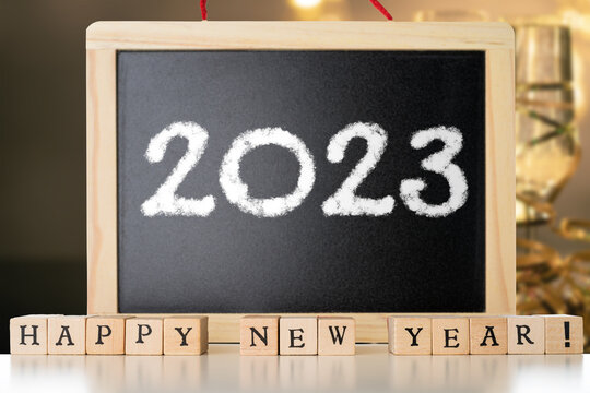 Blackboard with 2023 chalk text and happy new year made of wooden blocks witg festive champagne in the background. New Year's Eve concept