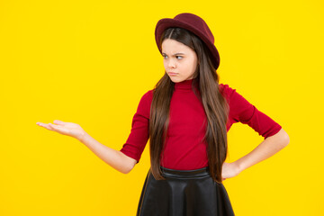 Angry face, upset emotions of teenager girl. Teenager child points aside with sad expression, shows amazing at blank empty space. Advertisement and mockup.