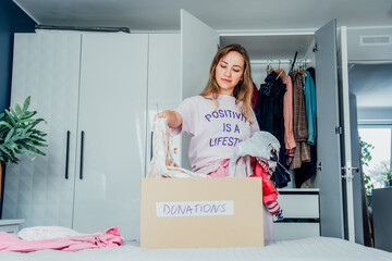 Woman selecting clothes from her wardrobe for donating to a Charity shop. Decluttering, Sorting clothes and Cleaning Up. Reuse, second-hand concept. Conscious consumer, sustainable lifestyle