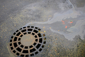 Oil spills of gasoline against the background of an asphalt road flow into a storm sewer.