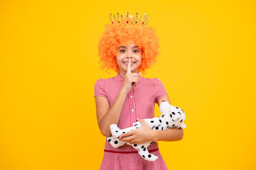 Teenager princess child in fancy clown wig hug toy. Teen girl in queen crown isolated on yellow...