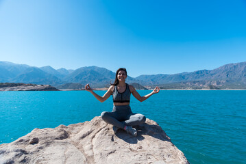 young and beautiful woman smiling, in a lake between mountains, yoga