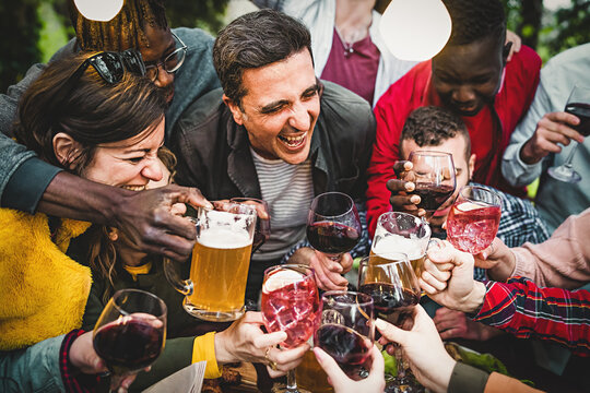 Group with many people celebrating a birthday toasting together with beers, wine and cocktails - a middle-aged man smiles in the middle of the fray - people and alcohol lifestyle concept