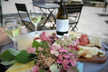 Gtazing board with assorted cheeses, meats, crackers, wne and bouquet of flowers for outdoor dining