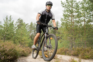 A man rides a mountain bike in a helmet and gear on the road in a green forest