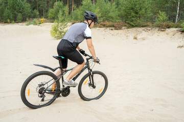 Fototapeta na wymiar Active sport a man rides a mountain bike in a helmet and equipment on the road in a green forest