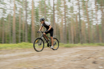 Naklejka premium Blurred in motion photo, a man fast on a mountain bike in helmet and gear on the road in the forest eco tourism
