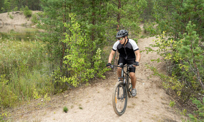 A man rides a mountain bike in a helmet and gear on the road in a green forest