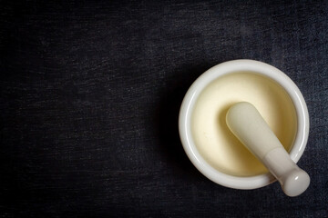 White ceramic mortar and pestle on black rustic wooden background, top view.