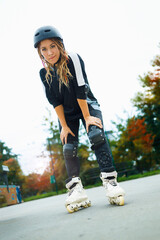 Young woman in roller blades enjoying her autumn day in a city skate park