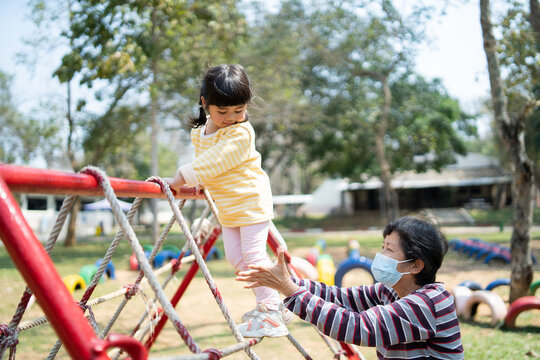 Cute asian girl and mother smile play on school or kindergarten yard or playground. Healthy summer activity for children. Little girl climbing outdoors playground. Child playing outdoor playground.