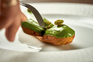 Eclair with pistachio glaze on a plate. Noise added in post-production. Selective focus