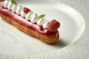 Eclair with berry glaze on a plate. Noise added in post-production. Selective focus