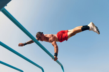 Workout. Strong muscular man, student training, practicing at sport ground at public park in summer morning, outdoors. Action, skills, challenges