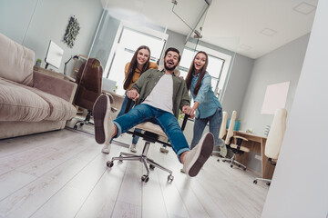 Full body photo of three childish employees push chair ride fast speed office indoors - obrazy, fototapety, plakaty