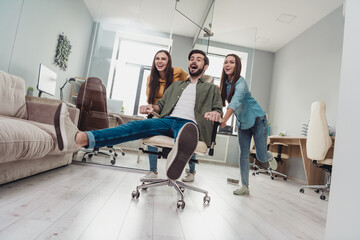 Full size photo of three overjoyed satisfied people playing enjoy pause break ride chair indoors