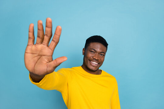 Photo of diversity funny guy raise arm towards you say hey see old friend wear yellow long sleeve shirt isolated blue color background